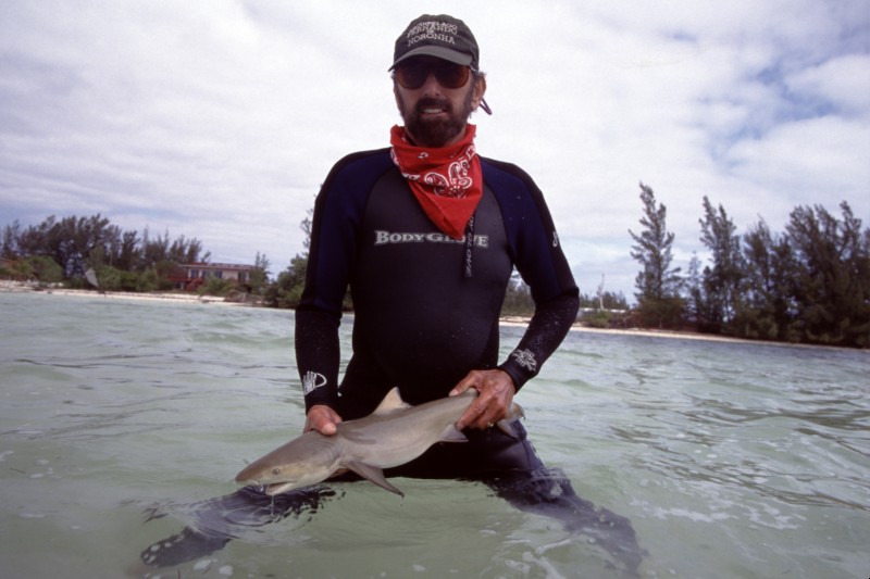 Dr. Samuel "Doc" Gruber stands in the water holding a small shark